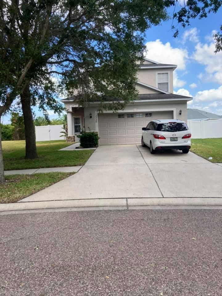 Two-story house with a driveway, a car parked in front, and a tree on a sunny day.