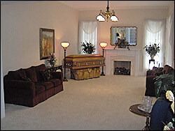 Funeral home viewing room with a casket, sofa, fireplace, and floral arrangements.