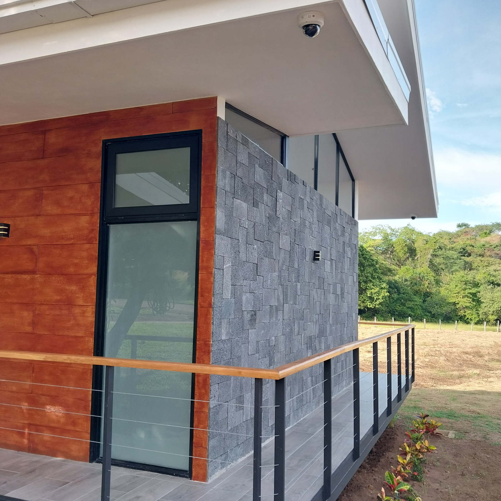 Exterior of modern building with wood paneling and stone wall. Balcony with black railing.