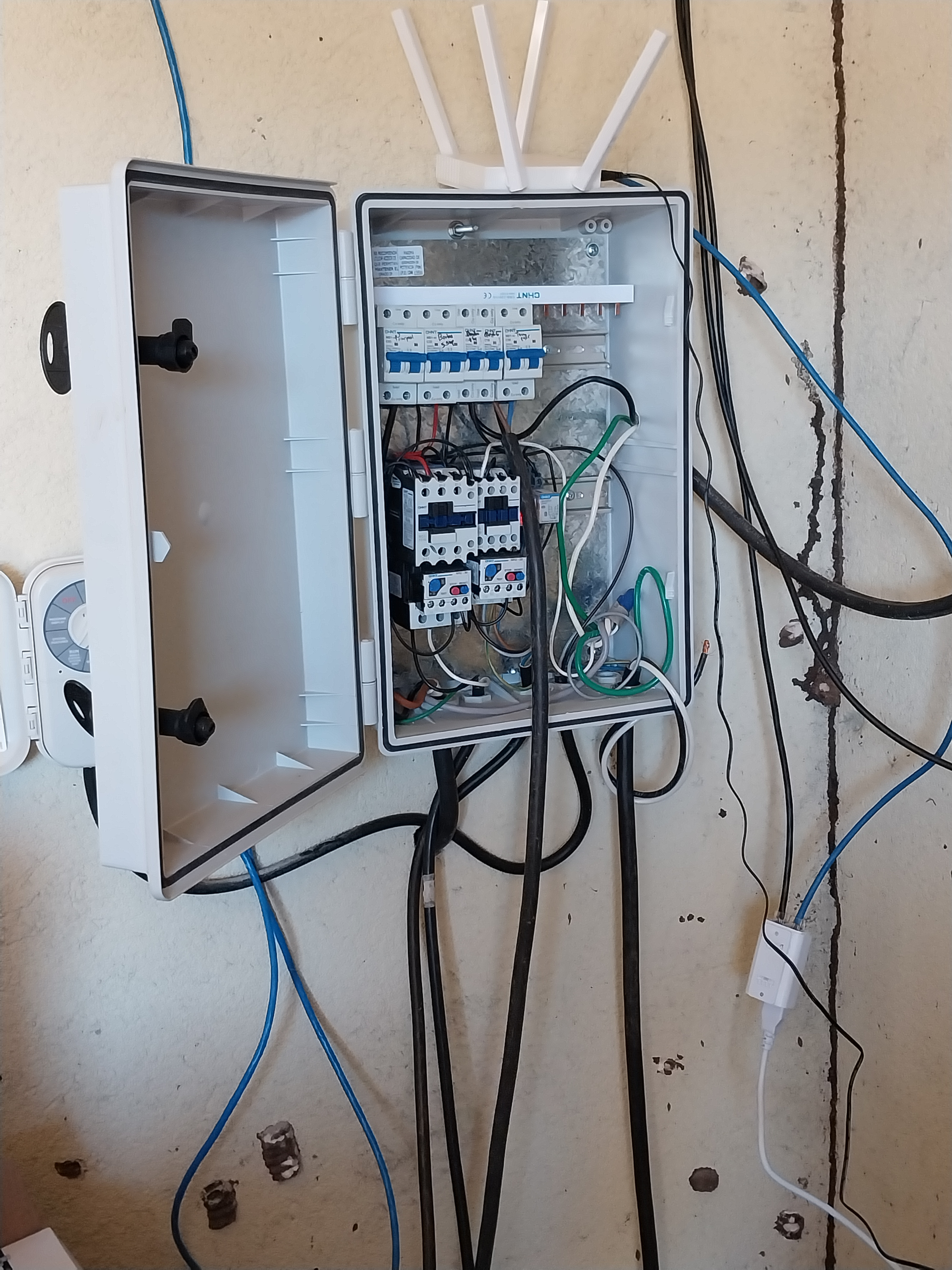 Electrical panel with wires and circuit breakers, mounted on a wall. Wi-Fi router antenna on top.