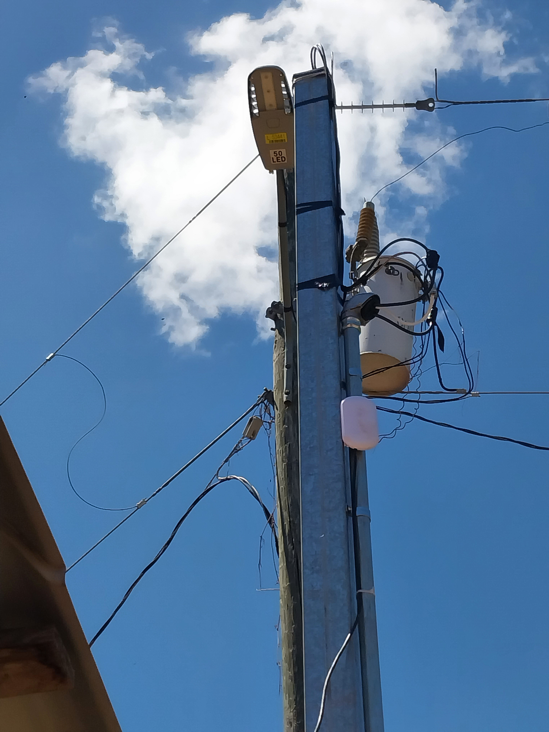 Utility pole with a transformer, wires, and a street light against a blue sky with clouds.