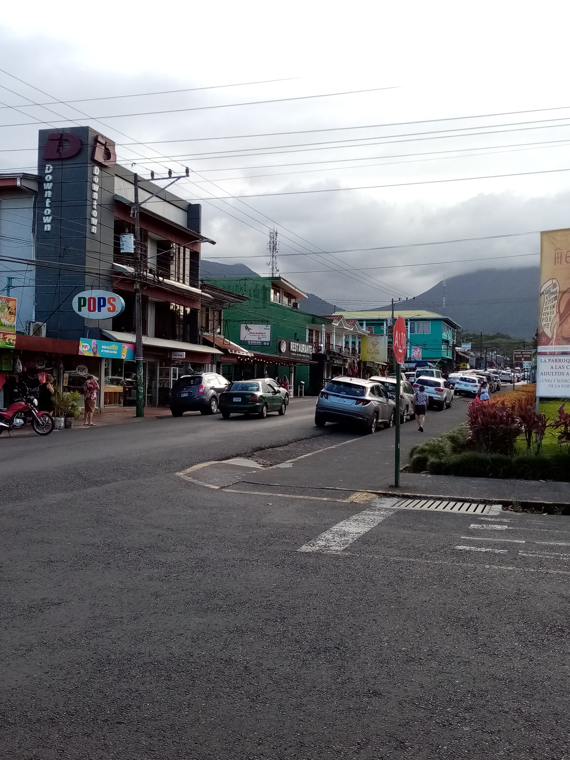 Street scene with cars, buildings, and mountains under a cloudy sky.