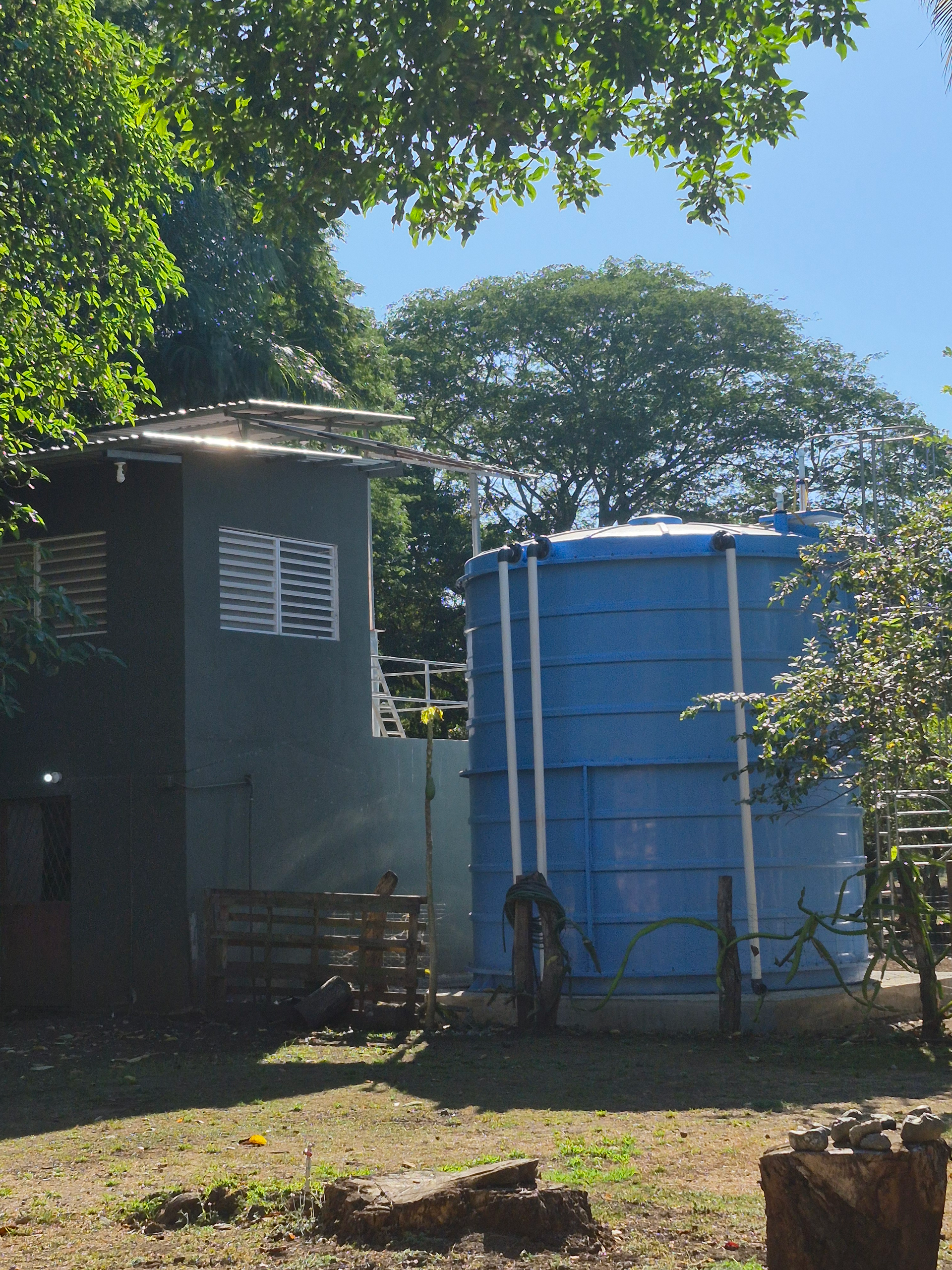 Blue water tank and small building outdoors, with trees in background.