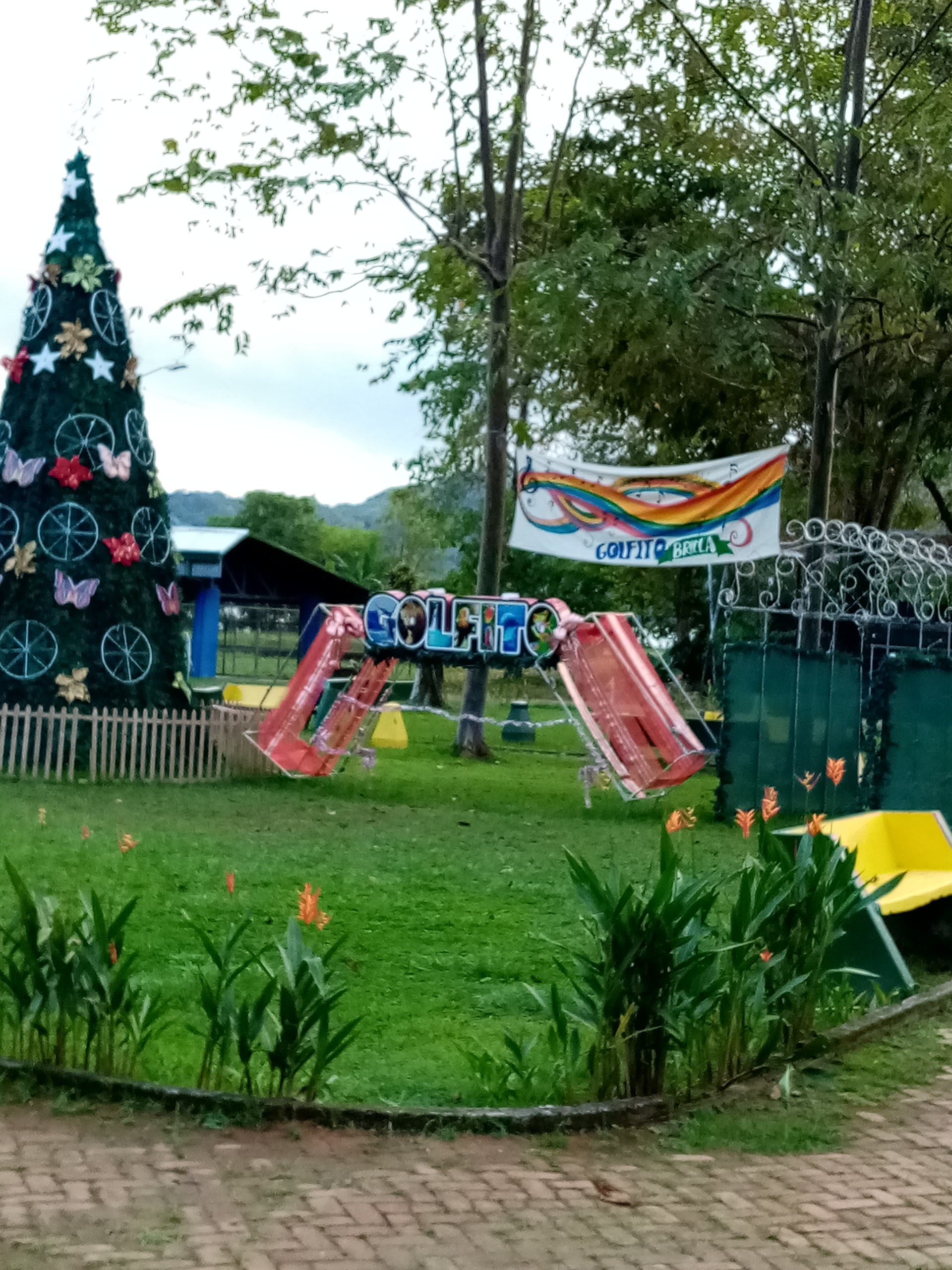 Playground with a Christmas tree, slide, and banner in a grassy area with trees.
