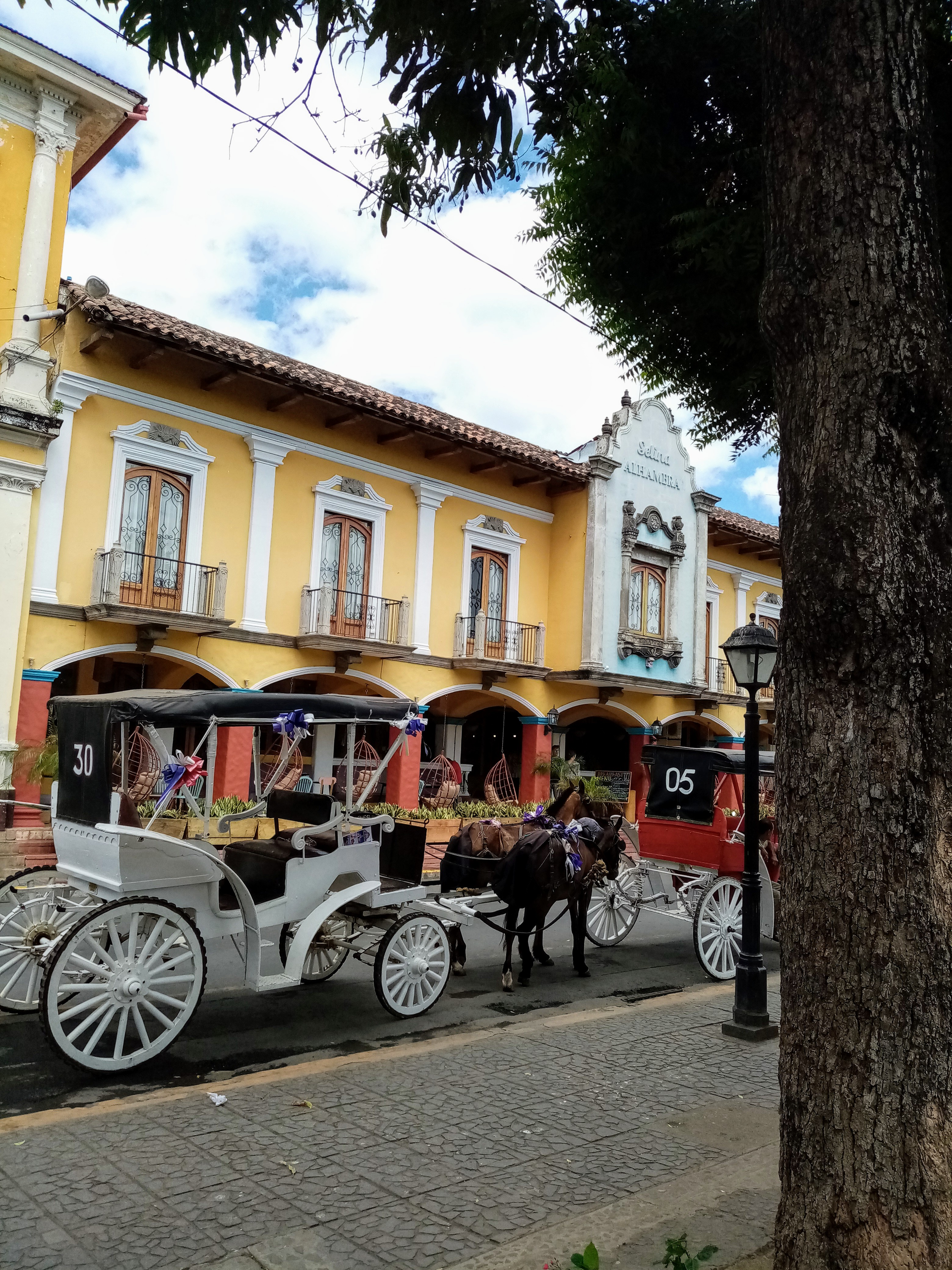 Two horse-drawn carriages parked in front of a yellow building with balconies. Cobblestone street, blue sky.