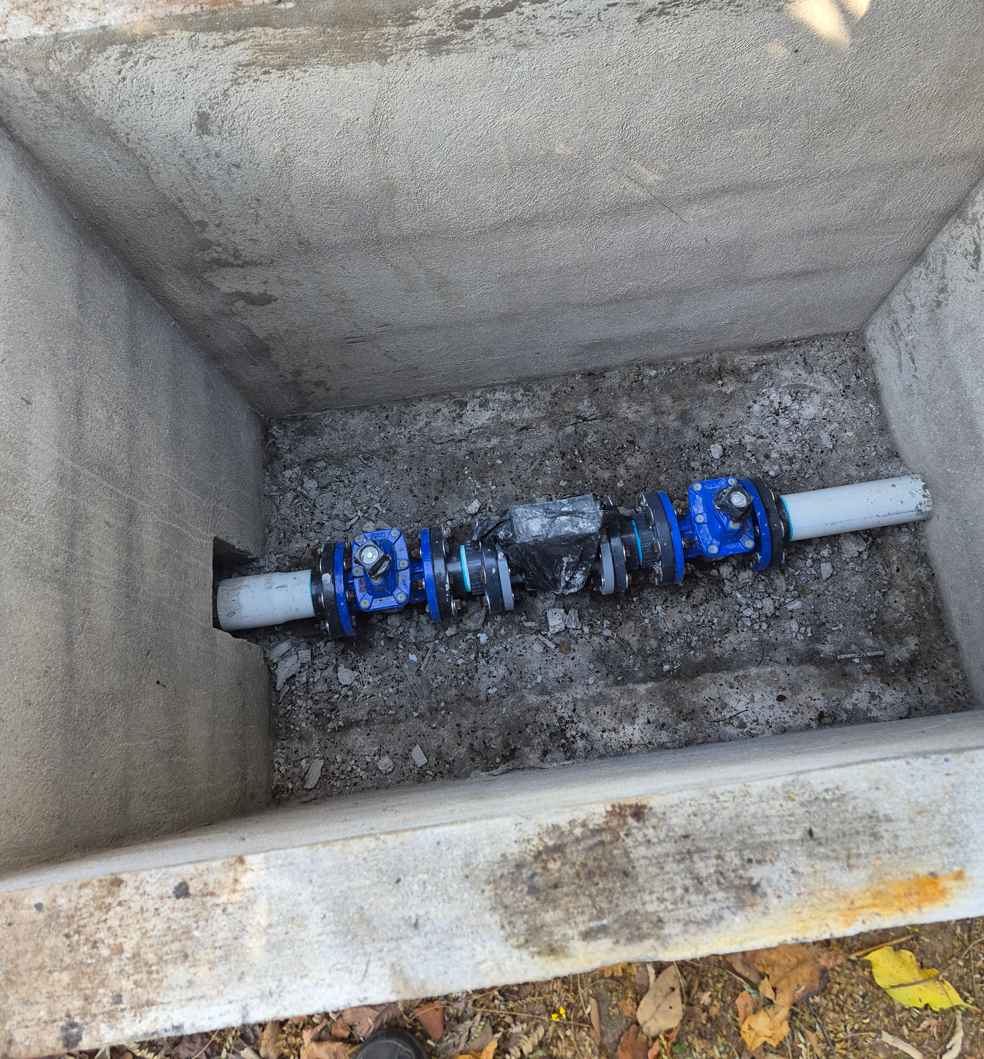 Pipes and blue valves inside a concrete box, likely for water control.