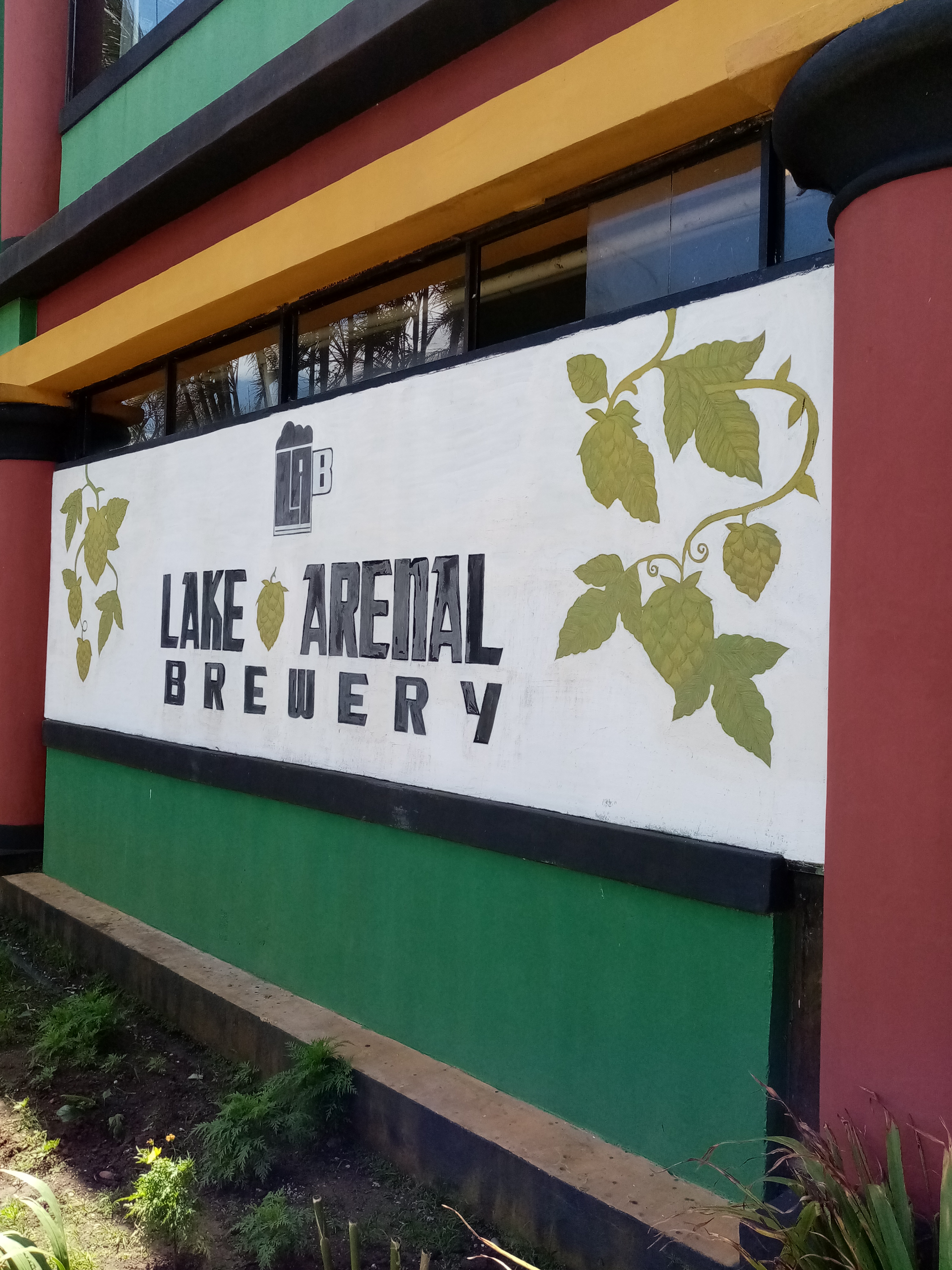 Sign for Lake Arenal Brewery; white with green and black text and hop vine decorations.