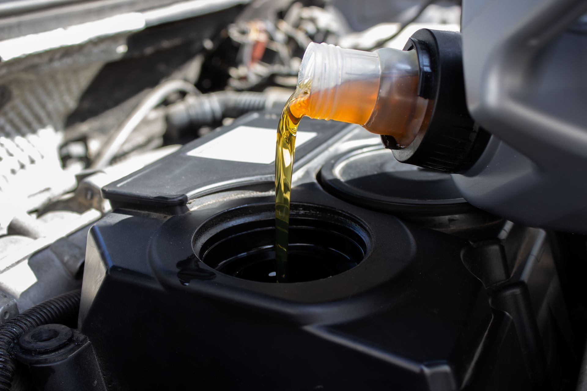 A close up of a person pouring oil into a car engine.