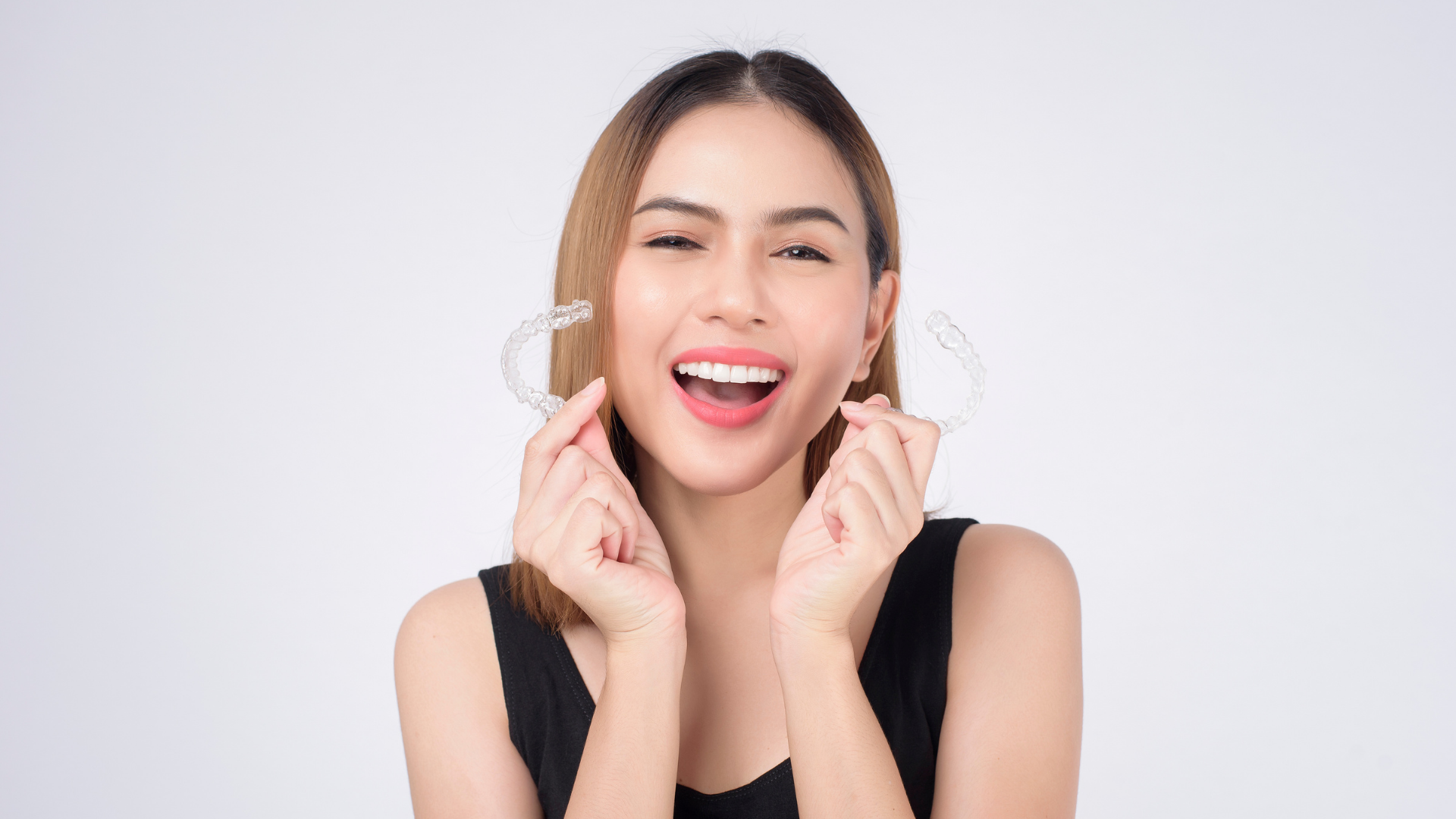 Woman smiling, holding clear dental aligners. Bright setting.