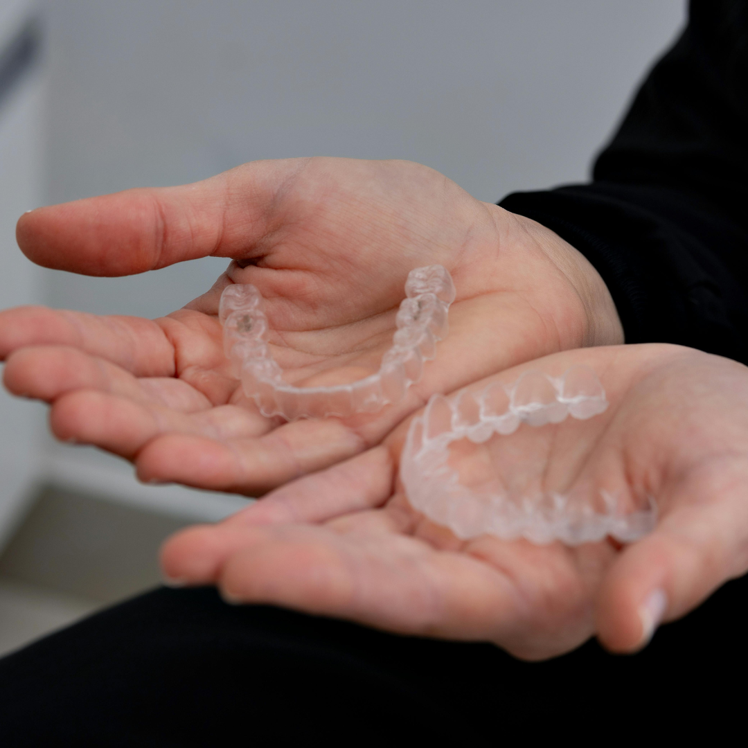Hands holding two clear aligners for teeth.