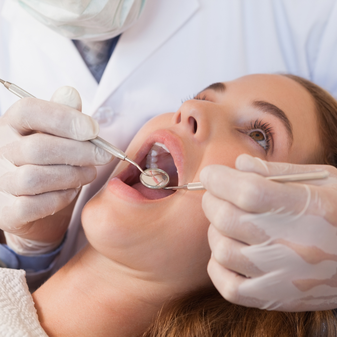 Dentist examining a woman's teeth with dental tools in a clinic.
