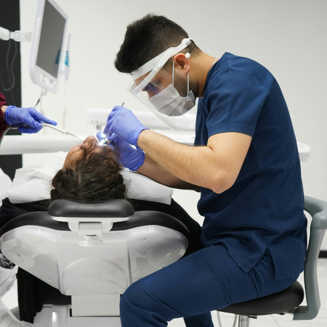 Dentist in blue scrubs, mask, and face shield working on a patient's teeth.