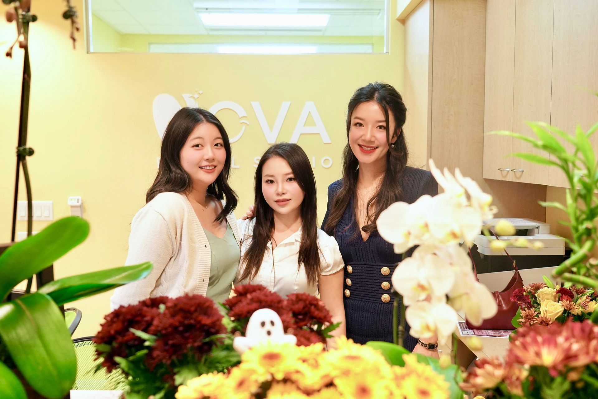 Three women are posing for a picture in front of flowers.