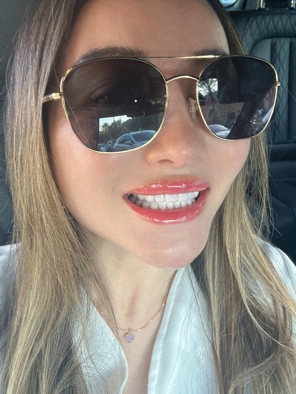 A woman wearing sunglasses and a necklace is smiling in a car.
