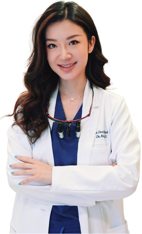 Woman wearing a white lab coat with dental loupes, smiling, arms crossed.