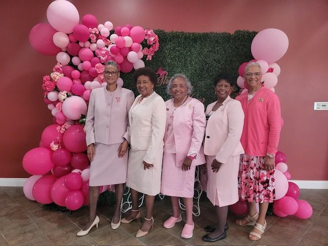 A group of women standing in front of a wall with pink balloons.