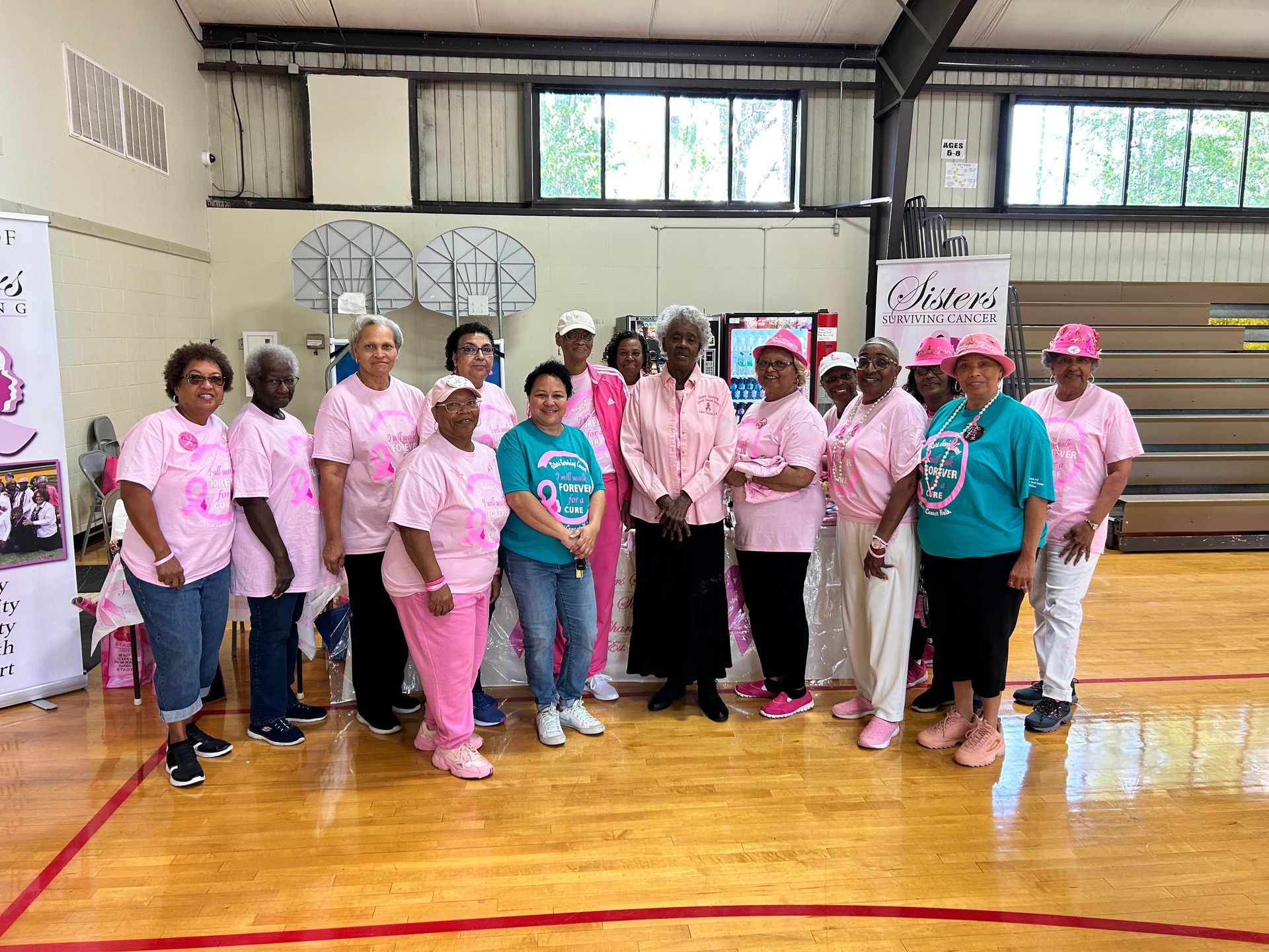 A group of women in pink shirts are posing for a picture in a gym.