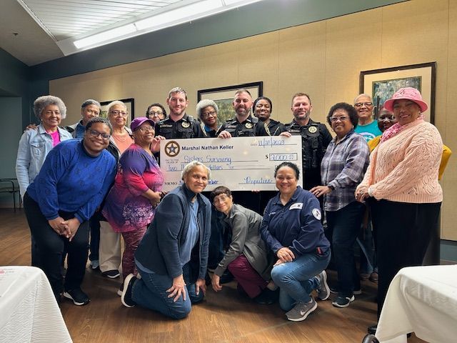A group of people are posing for a picture while holding a large check.