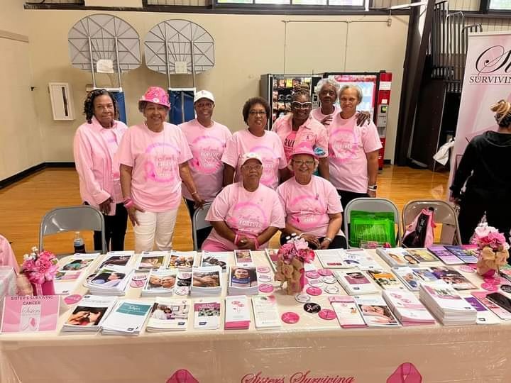 A group of women wearing pink shirts are standing around a table.