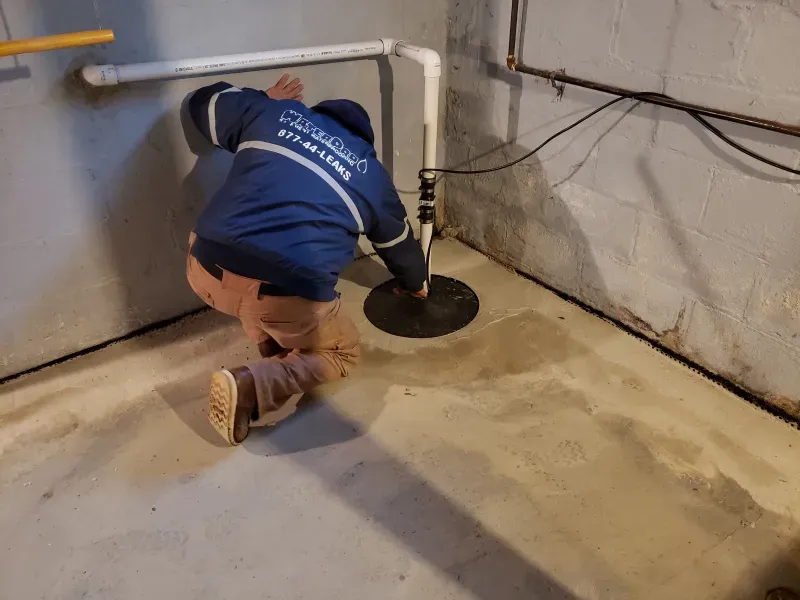 A man is kneeling down in a basement next to a pipe.