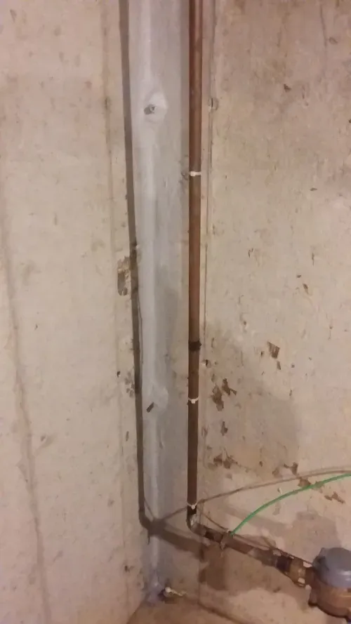 A close up of a pipe in a basement next to a wall.