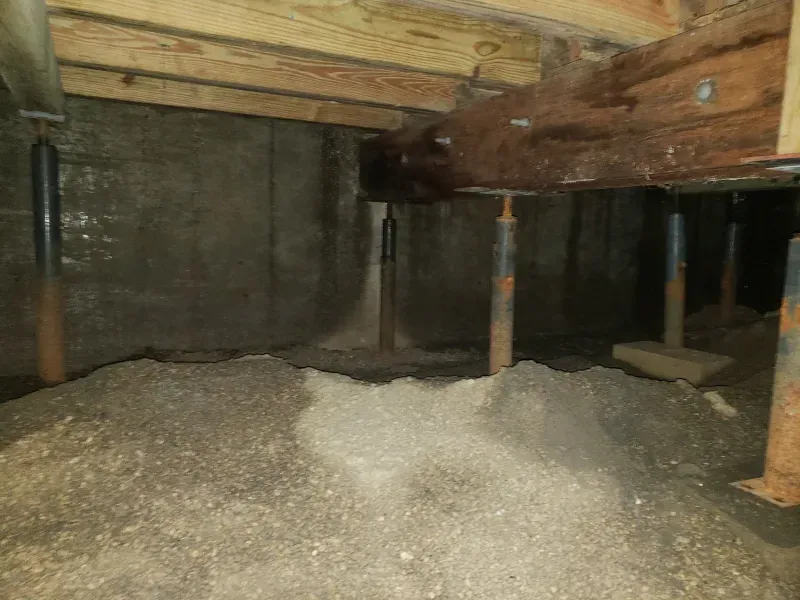 A pile of dirt is sitting under a wooden beam in a basement.