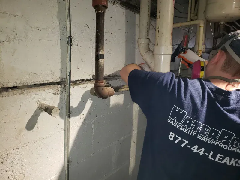 A man in a blue shirt is working on a pipe in a basement.