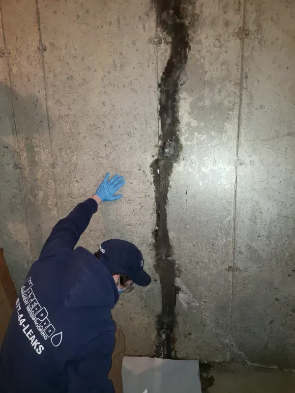 A man wearing blue gloves is standing in front of a concrete wall.