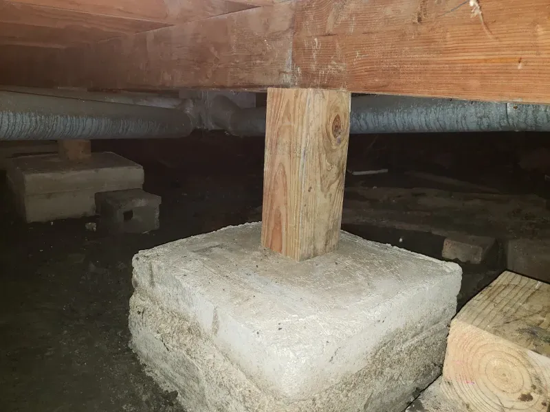 A wooden post is sitting on top of a concrete block under a wooden floor.