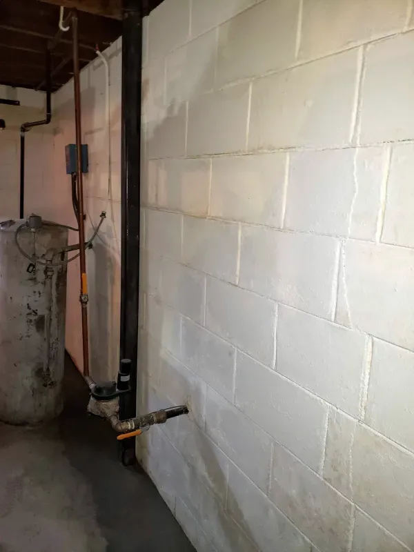 A white brick wall in a basement with pipes coming out of it.