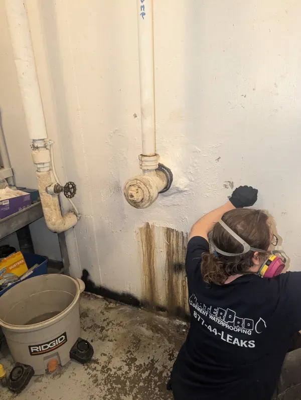 A woman is working on a pipe in a basement.