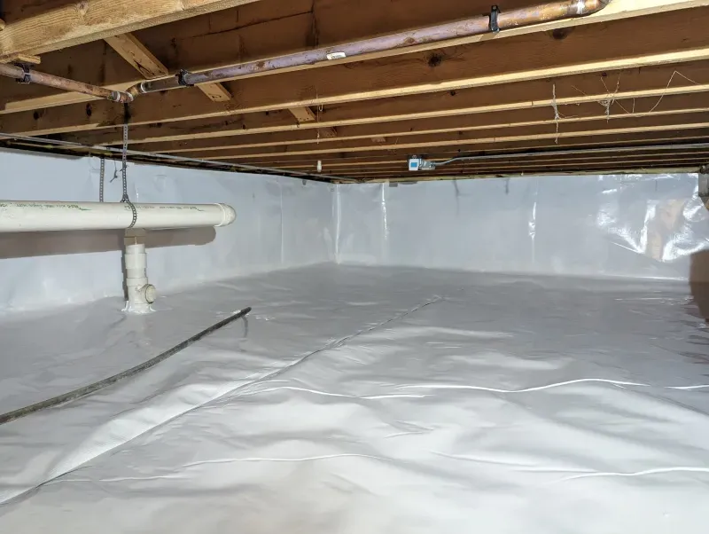 A basement with a plastic sheet on the floor and pipes.