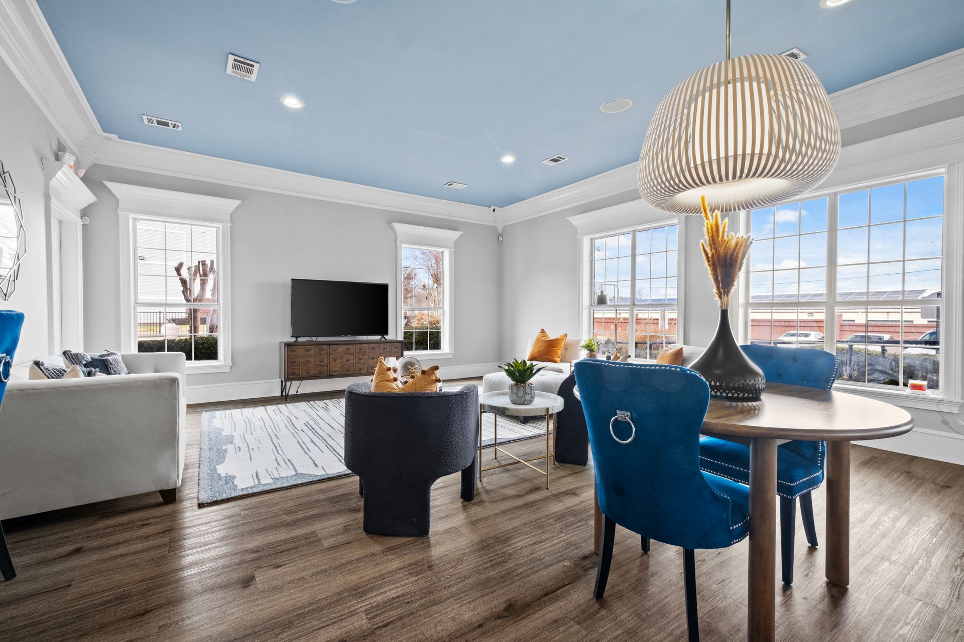 Open-concept living space: grey walls, dark wood floors, blue velvet chairs at kitchen island and dining table.