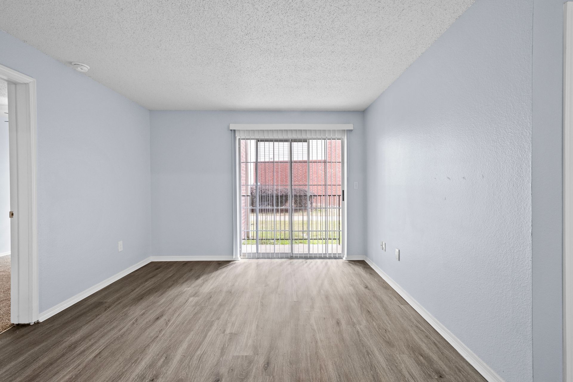An empty living room with hardwood floors and sliding glass doors at 73TwentyFive apartment in North Little Rock, AR.