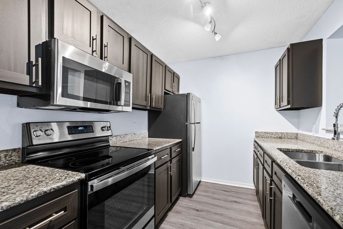 Kitchen with dark cabinets, stainless steel appliances, granite countertops, and light gray flooring.