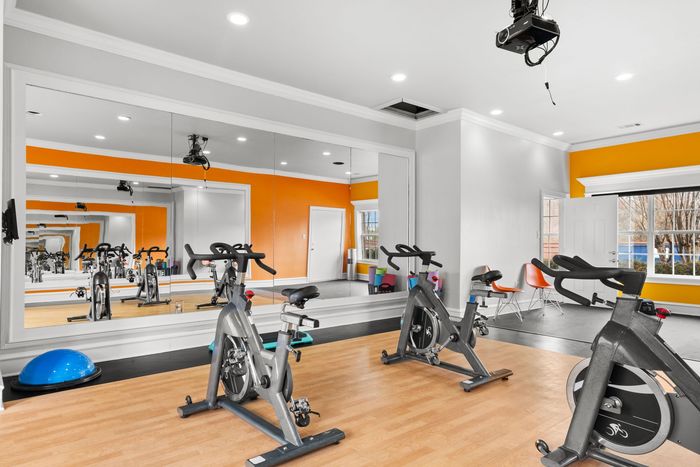 Spin class studio with stationary bikes, orange accent wall, and large mirror.