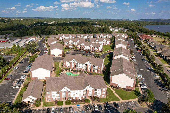 Aerial view of apartment complex with pool, parking, and surrounding trees and water.