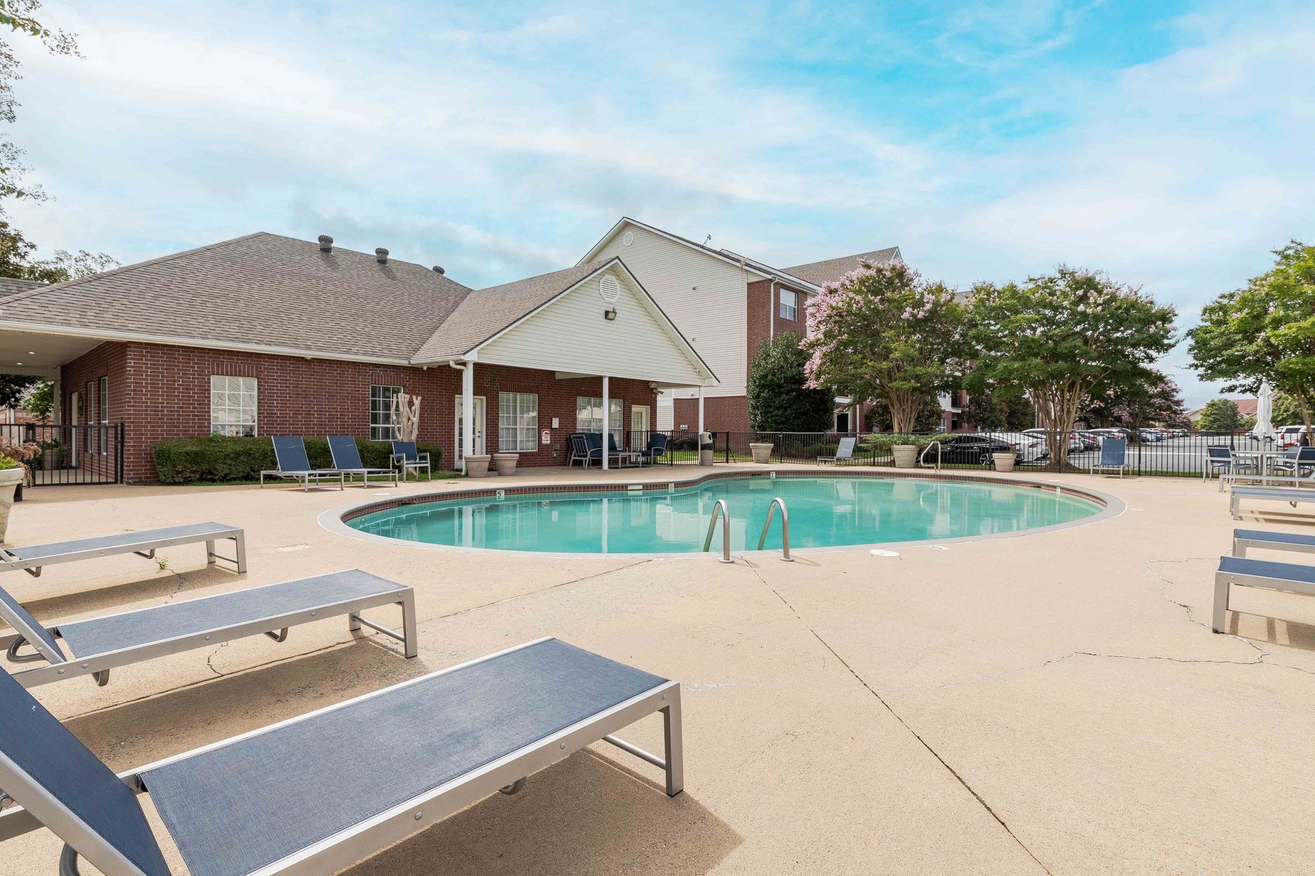 A large swimming pool surrounded by lounge chairs in front of a brick building at 73TwentyFive apartment in North Little Rock, AR.