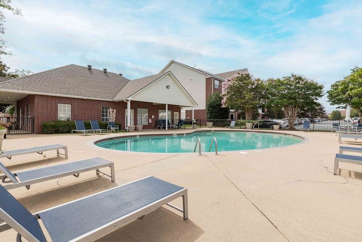 Swimming pool with lounge chairs in front of a brick building, sunny day.