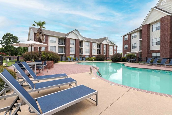 Apartment complex with pool, lounge chairs, and blue sky.