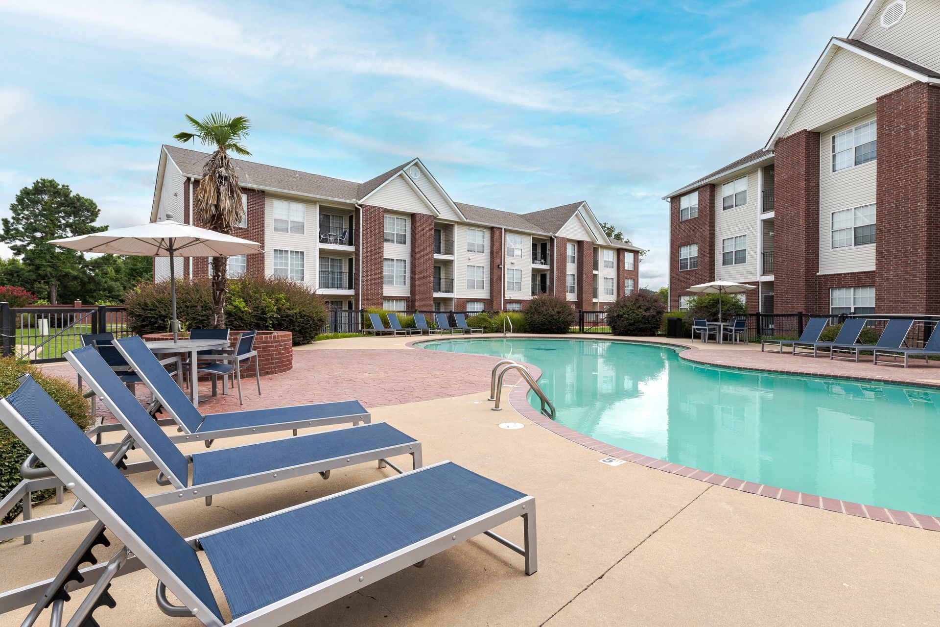 A large swimming pool surrounded by lounge chairs and umbrellas in front of a brick building at 73TwentyFive.