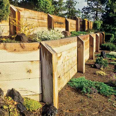 A wooden fence is surrounded by plants and rocks in a garden.