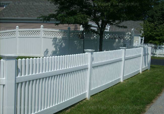 A white picket fence surrounds a lush green yard in front of a house.