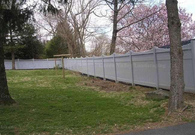 A white fence surrounds a lush green field with trees in the background.