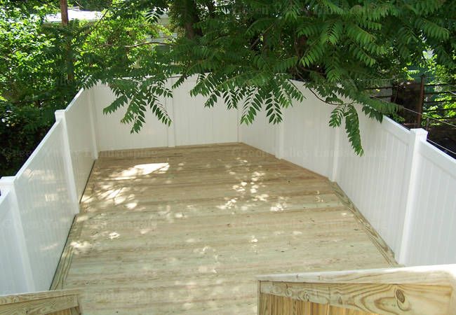 A wooden deck with a white fence and a tree in the background.