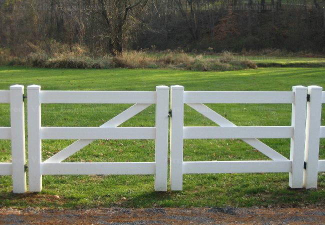 A white fence surrounds a grassy field with trees in the background.