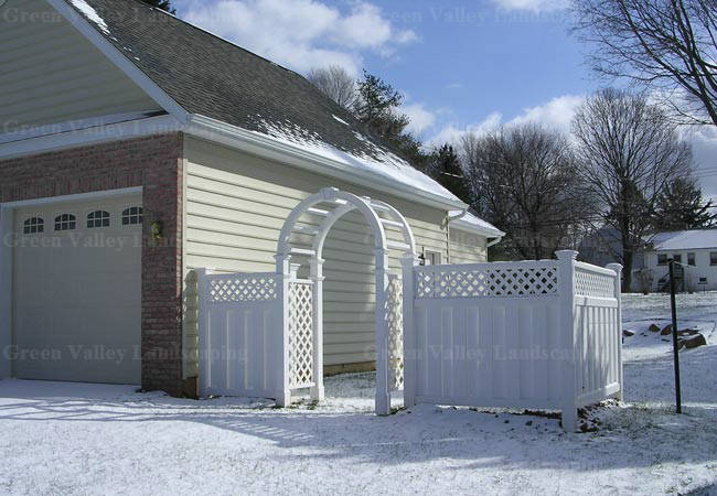 A white fence is in front of a house in the snow