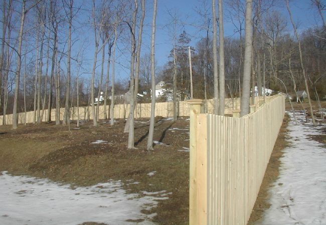 A wooden fence is surrounded by trees in a snowy field.