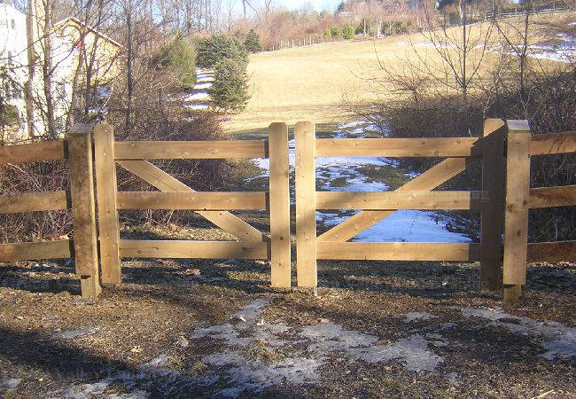 A wooden fence surrounds a field with a house in the background