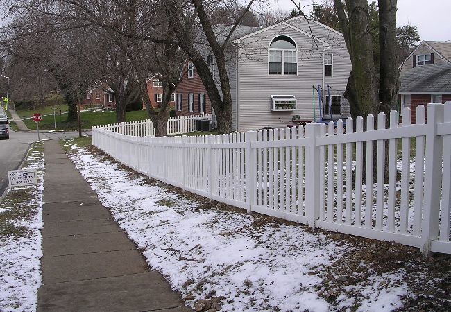 A white picket fence along a sidewalk in front of a house
